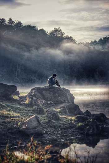 man in gray shit sitting on rock boulder