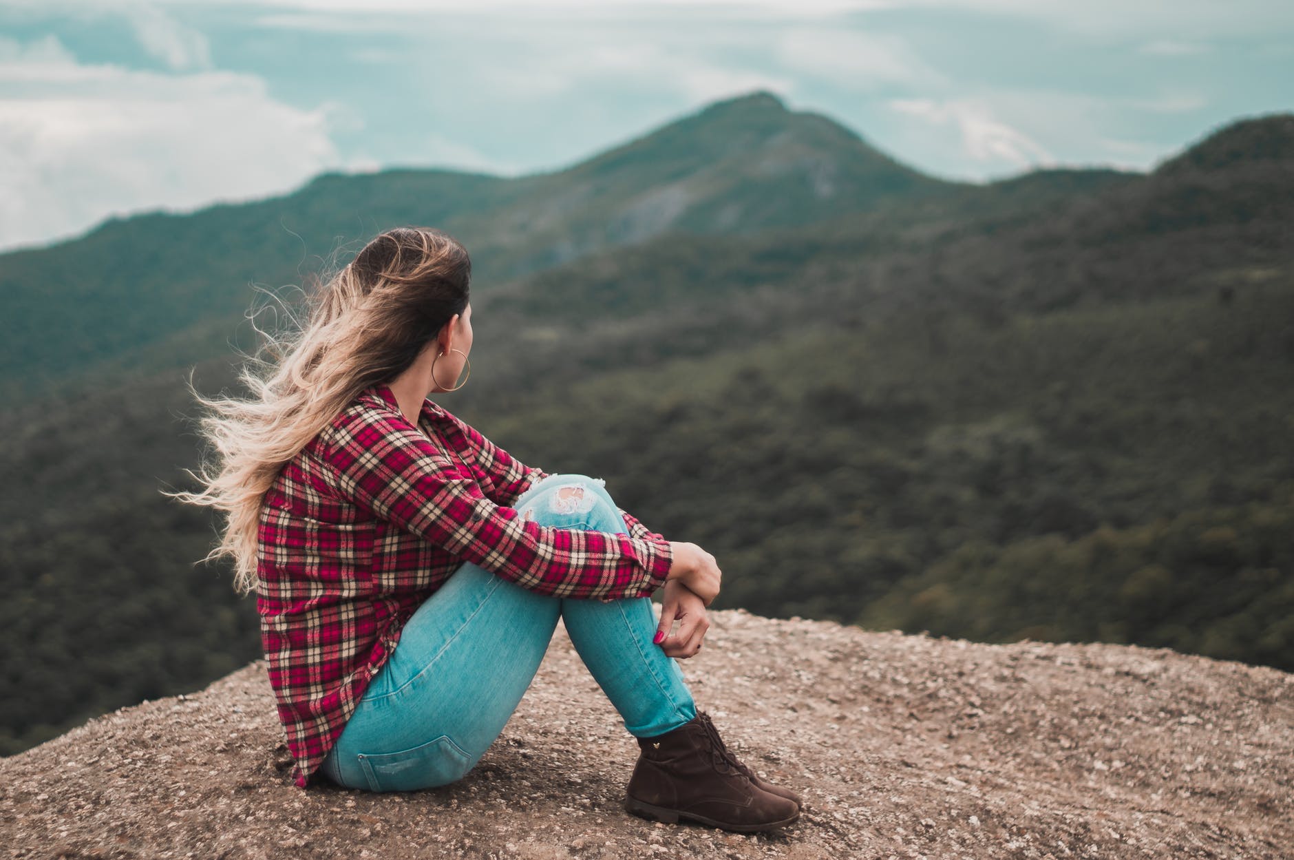 side view photo of woman sitting on ground overlooking a hill