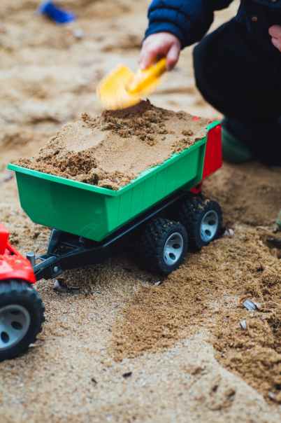 child playing sand with shovel and truck toy