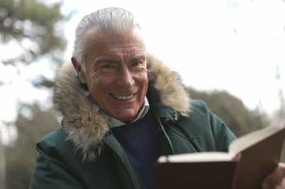 man in green winter jacket holding a brown book