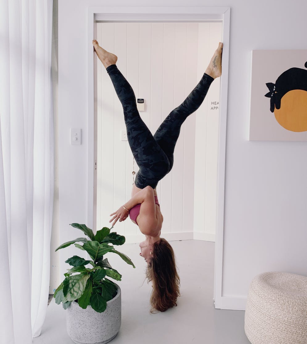woman in workout gear hanging upside down on doorway near green plants